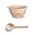 Cream ceramic mixing bowl with cute bear and donut design and matching ceramic spoon on white background.