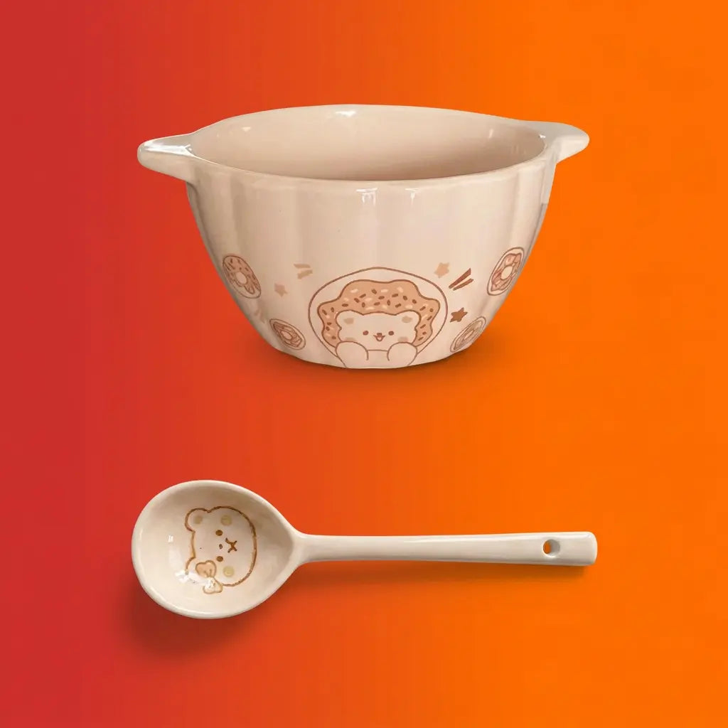 Cream ceramic mixing bowl with cute bear and donut design and matching ceramic spoon on orange-red gradient background.