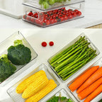 Set of clear refrigerator storage bins with built-in handles holding broccoli, corn, and carrots