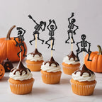 Black skeleton cupcake toppers in cupcakes with orange pumpkins nearby