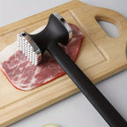 Meat tenderizer mallet on steak with a ribbed metal head and black handle