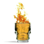 Skull head shot glass with amber drink and flames, clear skull face on front