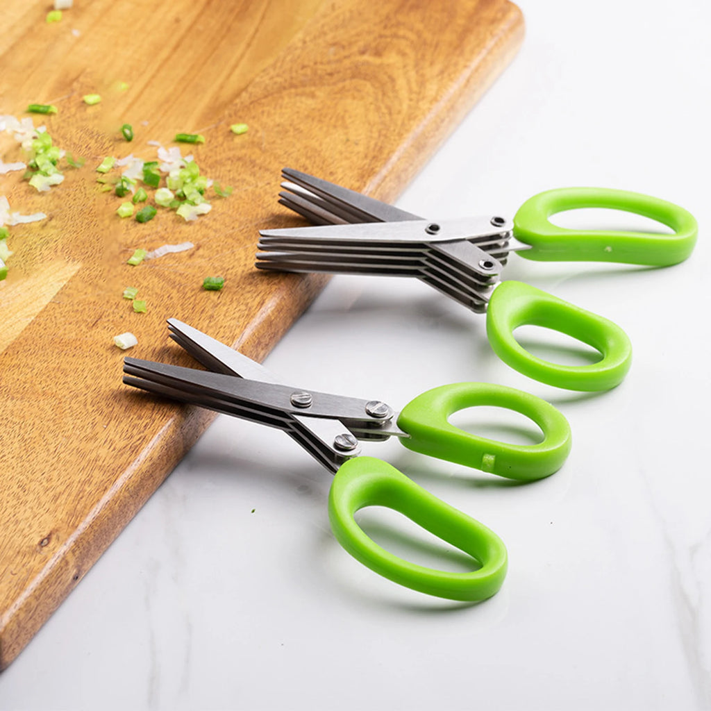 Stainless multi-blade herb shears with green handles on a board with chopped herbs
