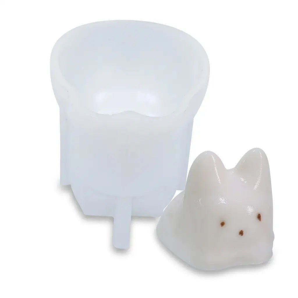 White silicone cat candle mold next to a white cat-shaped candle with brown spots on white background.