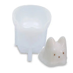 White silicone cat candle mold next to a white cat-shaped candle with brown spots on white background.