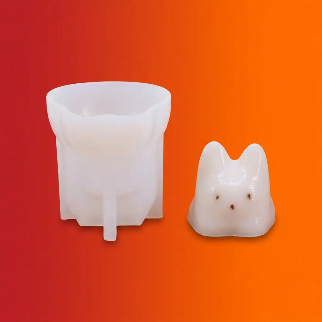 White silicone cat candle mold next to a white cat-shaped candle with brown spots on orange background.
