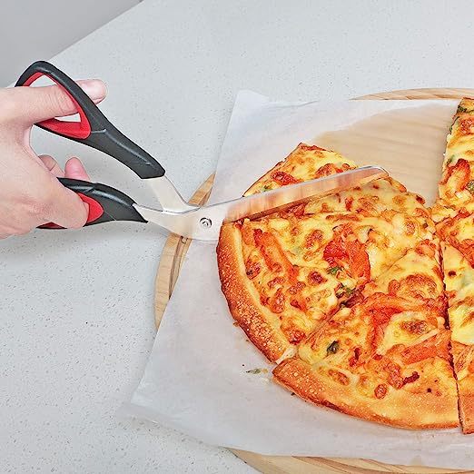 Hand using black and red pizza scissors to cut a cheese pizza on parchment paper