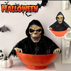 Orange skull bowl haunted house prop with hooded skeleton face, arms over the rim