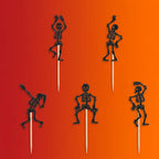 Five black glitter skeleton Halloween food picks on sticks on orange-red gradient background.