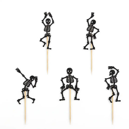 Five black glitter skeleton Halloween food picks on sticks on white background.