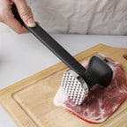 Meat tenderizer mallet with black handle pounding steak on a cutting board