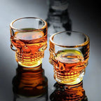 Two amber skull head shot glasses with raised skull face details and filled liquid