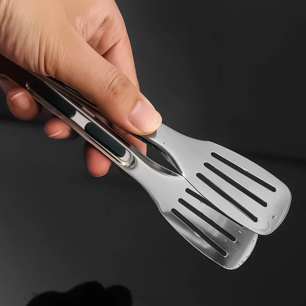 Stainless steel cooking tongs with slotted head and green silicone grip, held in hand