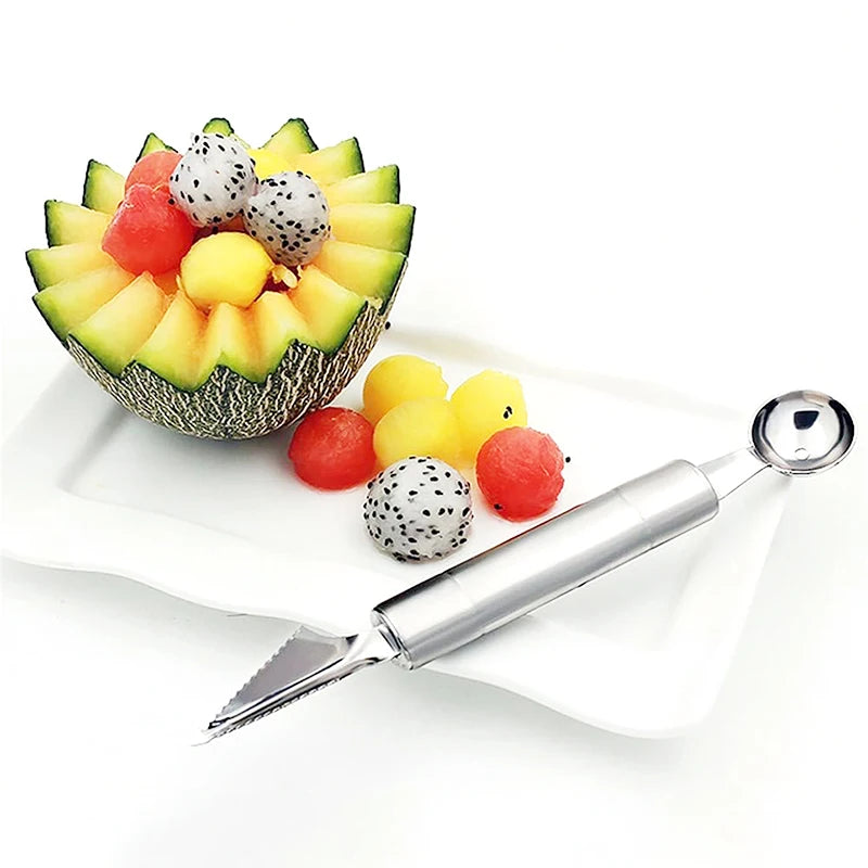Stainless steel melon baller and carving tool with pointed tip resting on fruit platter