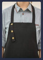 Dark canvas chef apron with brass button strap and front pocket panel