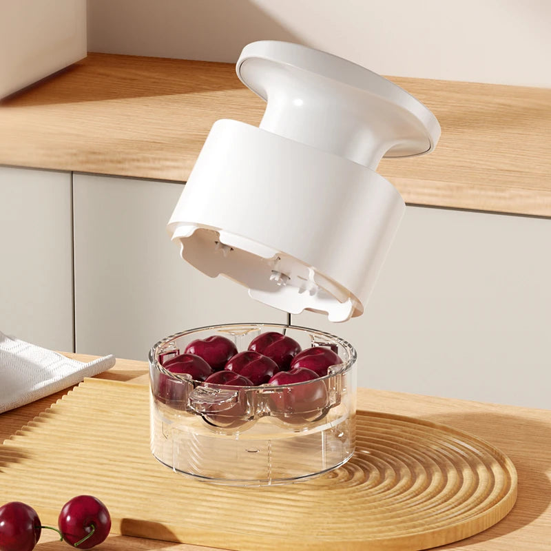 White cherry pitter dispensing cherries into a clear bowl; multi-hole chamber on base