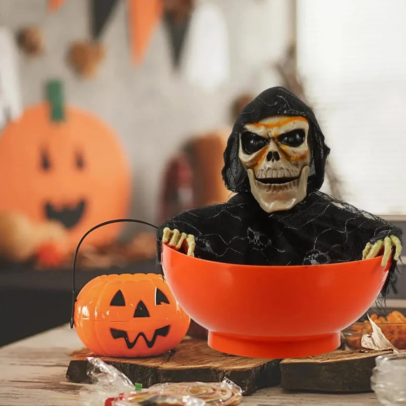 Orange skull bowl haunted prop with hooded skeleton face beside carved pumpkin