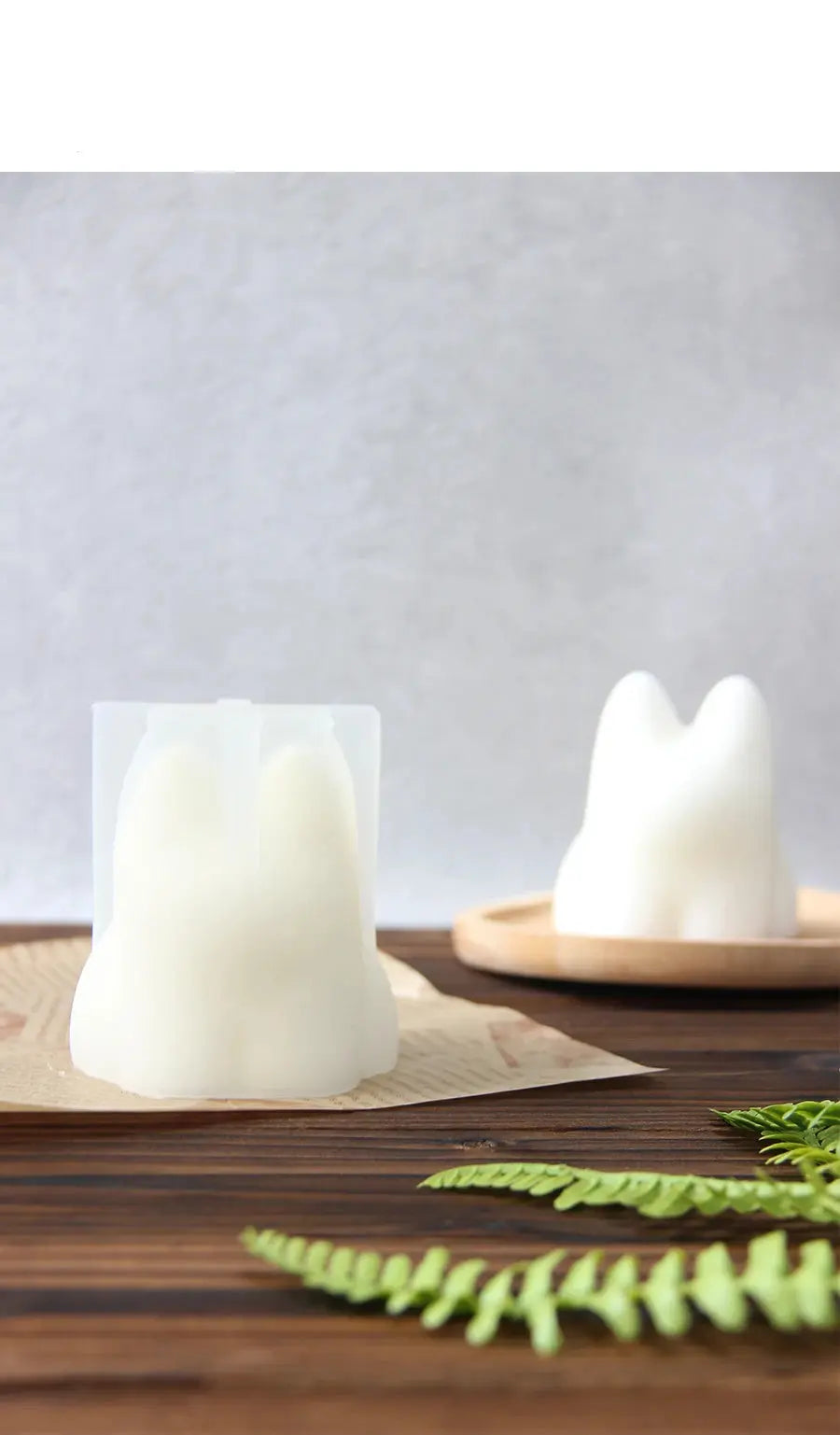 White silicone mold and molded candle or soap shaped like a tooth on a wooden surface with fern leaves.