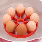 Red silicone steamer rack with nine eggs positioned in a pan