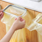 Grey over-cabinet trash bag holder with yellow liner clipped over the underside