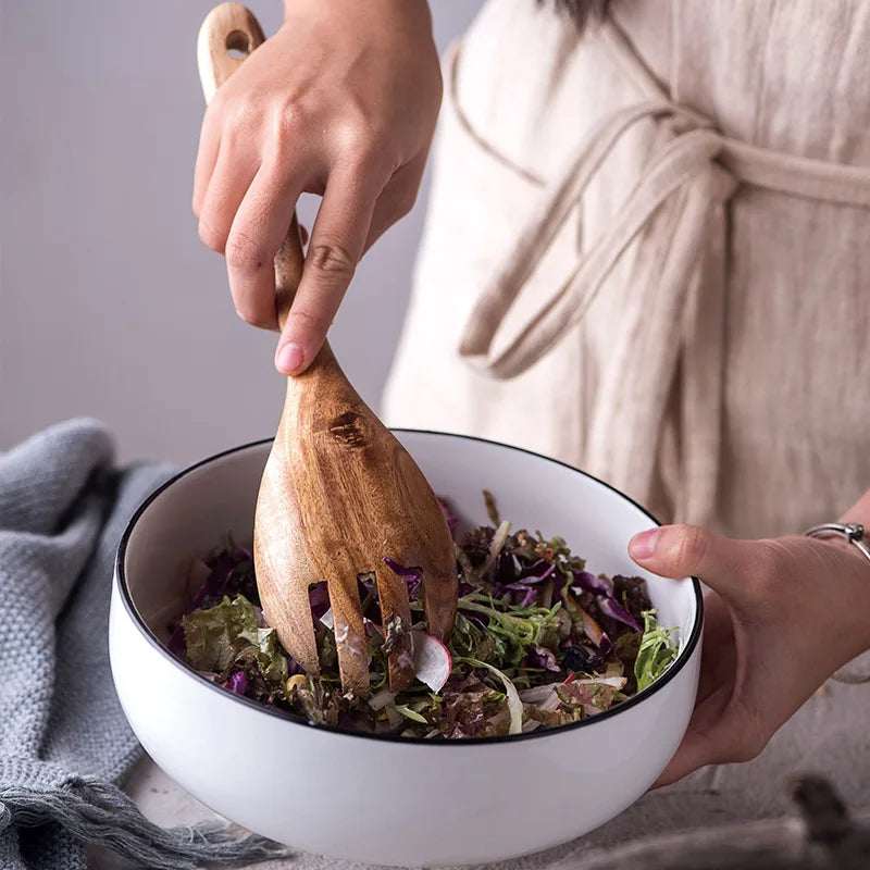 Acacia wood salad servers lifting greens from a bowl, spoon and slotted fork