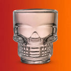 Clear glass skull-shaped Halloween drinking cup on orange-red gradient background.
