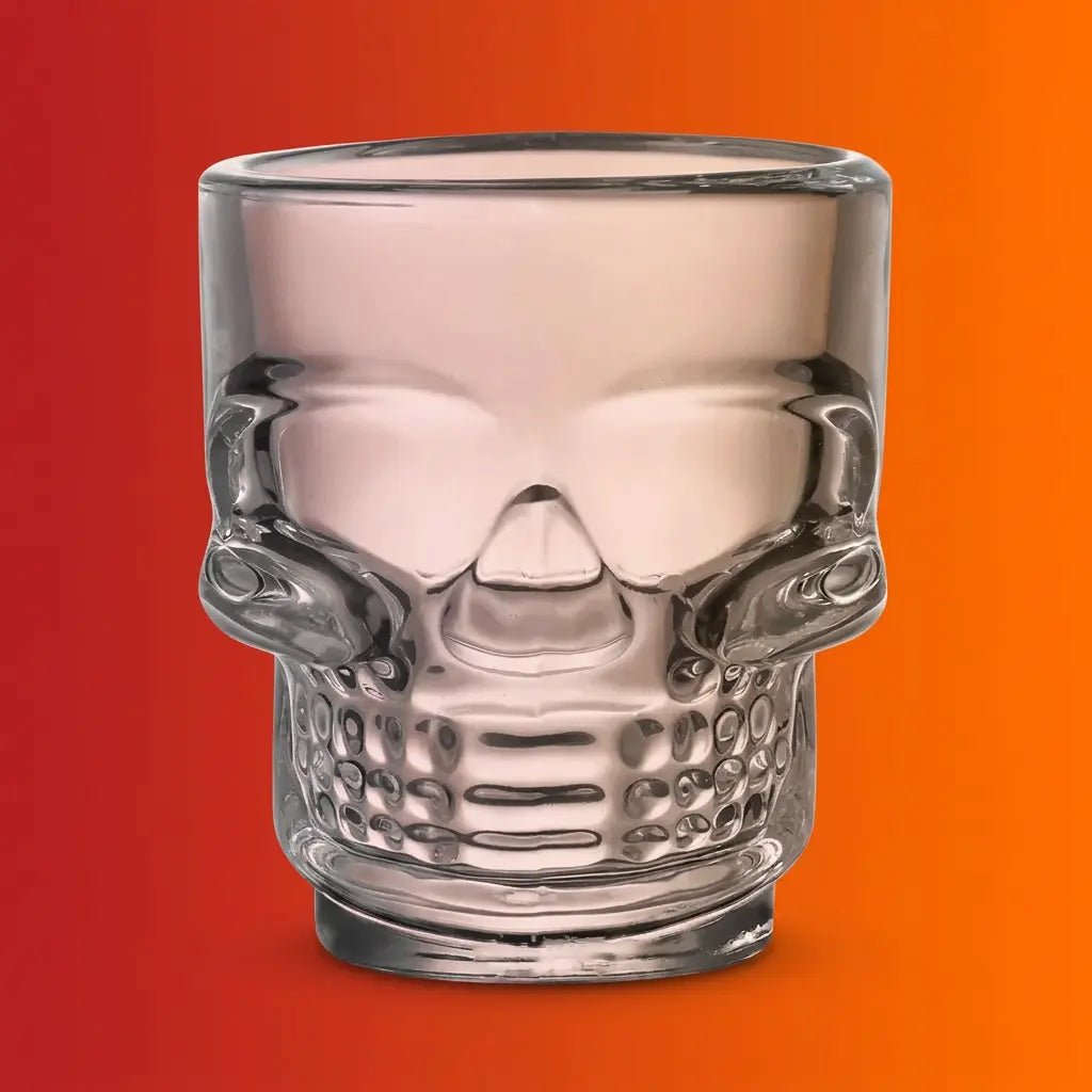 Clear glass skull-shaped Halloween drinking cup on orange-red gradient background.