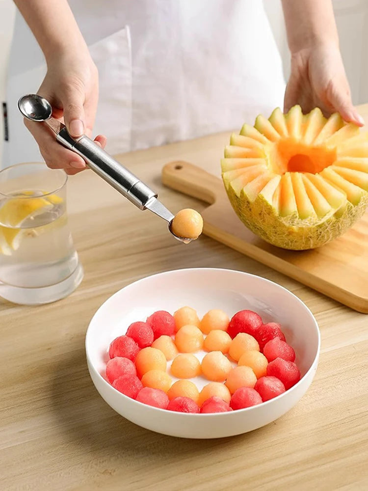 Stainless steel fruit baller with light handle scooping melon balls beside a bowl