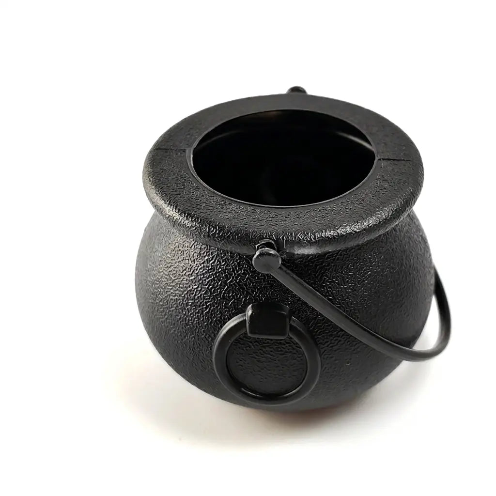 Black cast iron Halloween witch cauldron with a metal handle on white background.