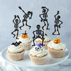 Black skeleton cupcake toppers on sticks with frosted cupcakes on a serving plate