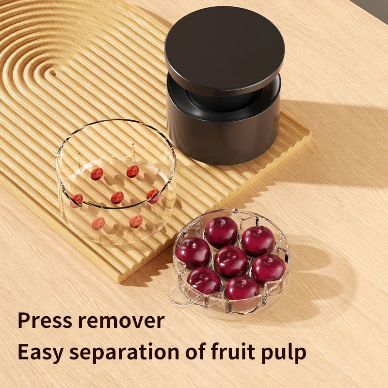 Black cherry pitter with clear chamber and round press lid; press remover beside cherries