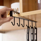 Under-cabinet 6-hook mug hanger, hand sliding the matte black rack onto a shelf