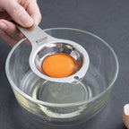 Stainless steel egg separator over bowl, yolk in metal cup, lifting by handle