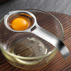 Stainless steel egg yolk separator with bowl rest hook, holding one egg yolk in bowl
