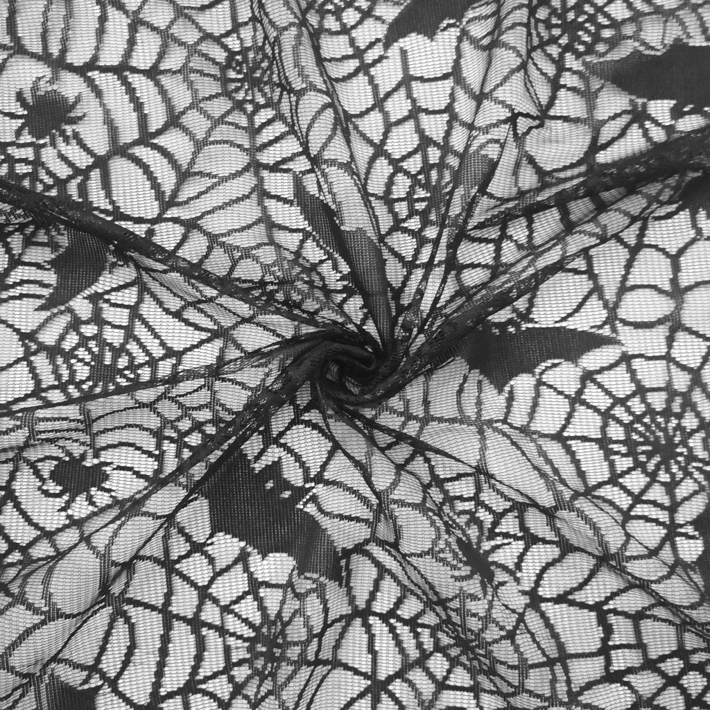 Close-up texture detail of black lace Halloween tablecloth showing spider web and bat pattern.