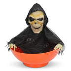 Halloween grim reaper skeleton figure wearing black hooded robe emerging from orange candy bowl on white background.