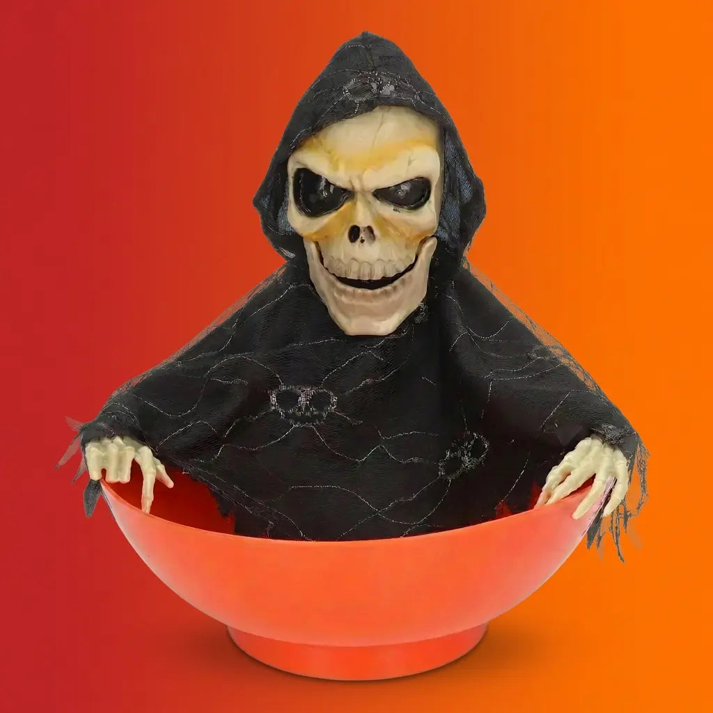 Halloween grim reaper skeleton figure wearing black hooded robe emerging from orange candy bowl on orange-red gradient background.