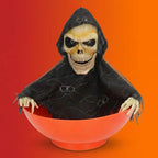 Halloween grim reaper skeleton figure wearing black hooded robe emerging from orange candy bowl on orange-red gradient background.